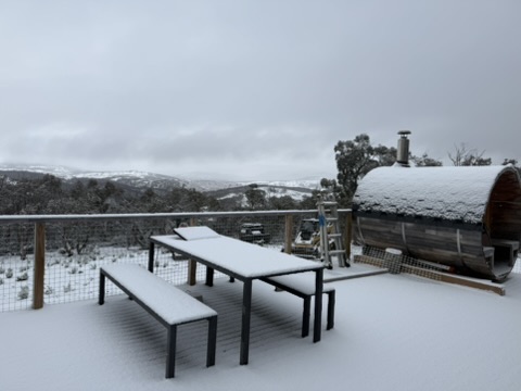 Snow settling on the deck and wood-fired tub, with the valley beyond.